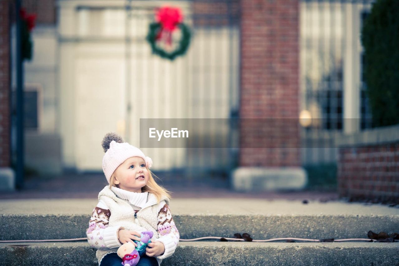 Smiling baby girl in warm clothing looking away while sitting on steps