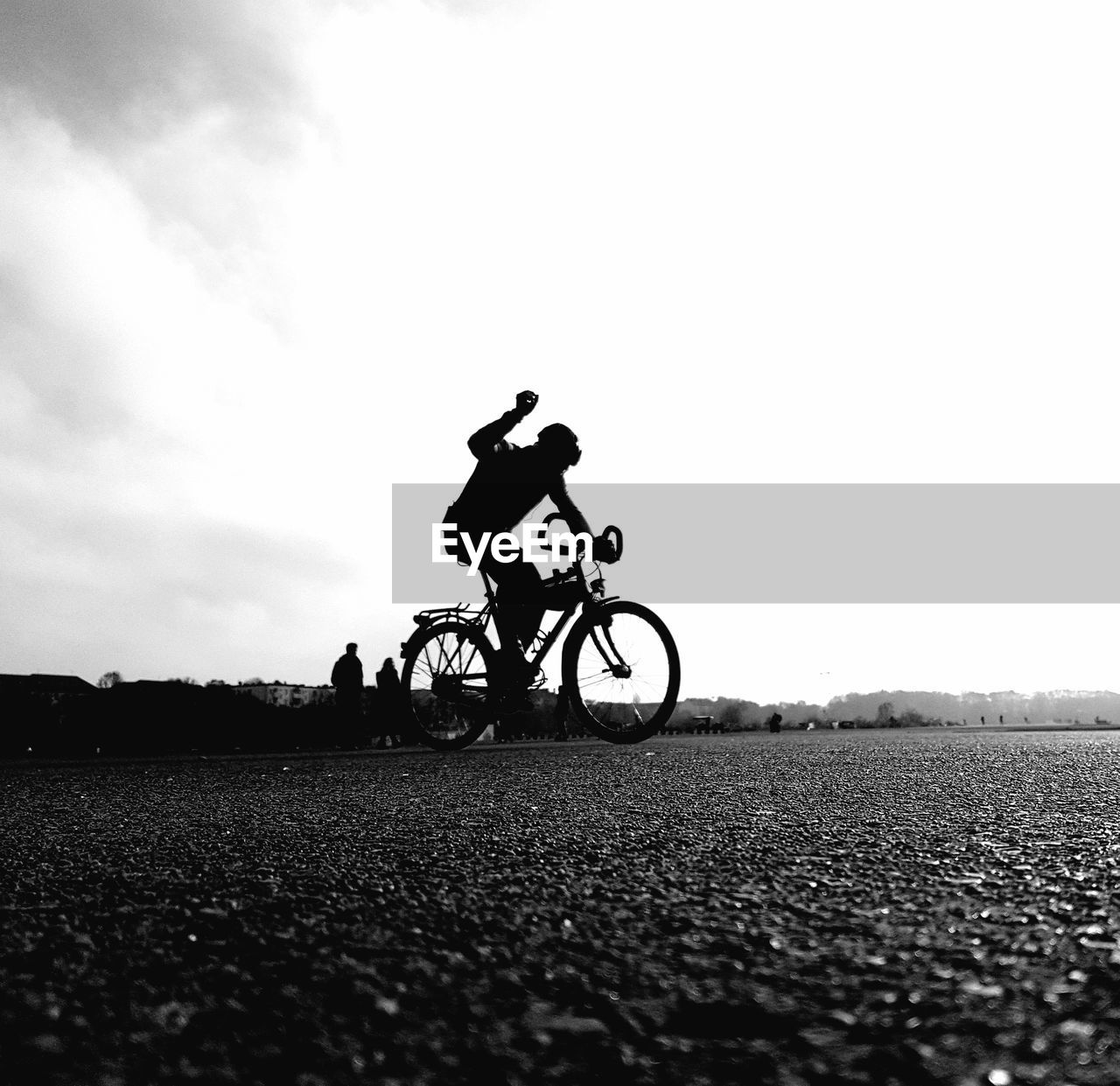 MAN RIDING BICYCLE BY ROAD AGAINST SKY