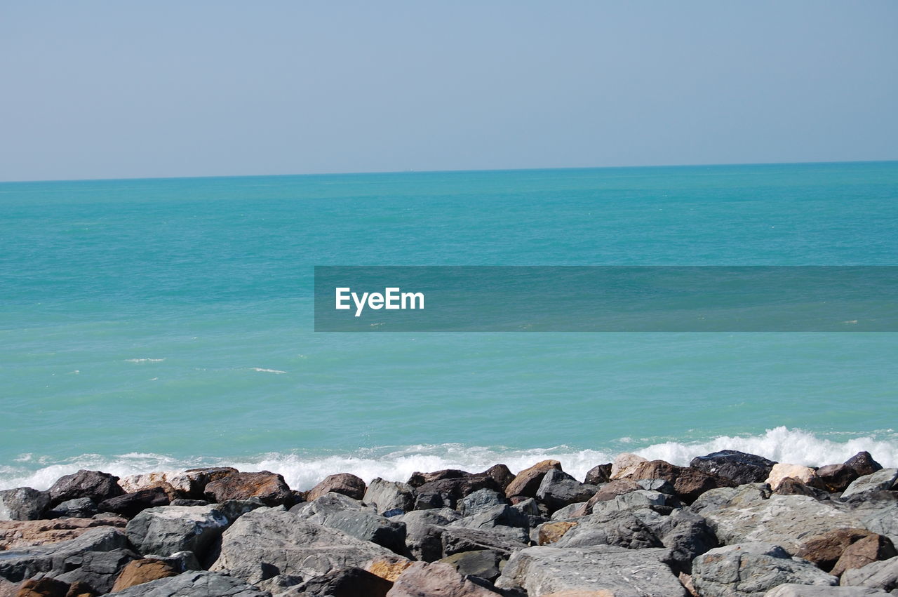 ROCKS BY SEA AGAINST CLEAR SKY
