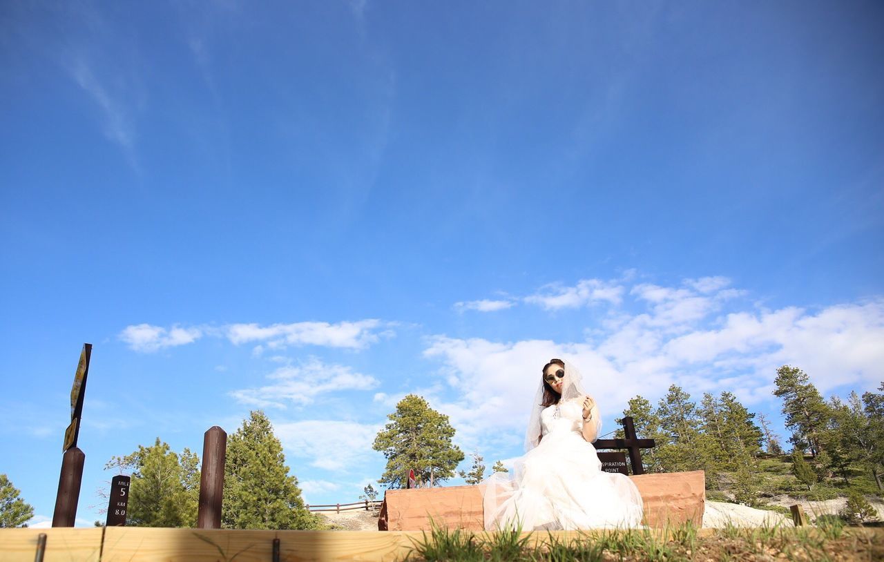 Bride in sunglasses sitting on bench against blue sky at bryce canyon national park