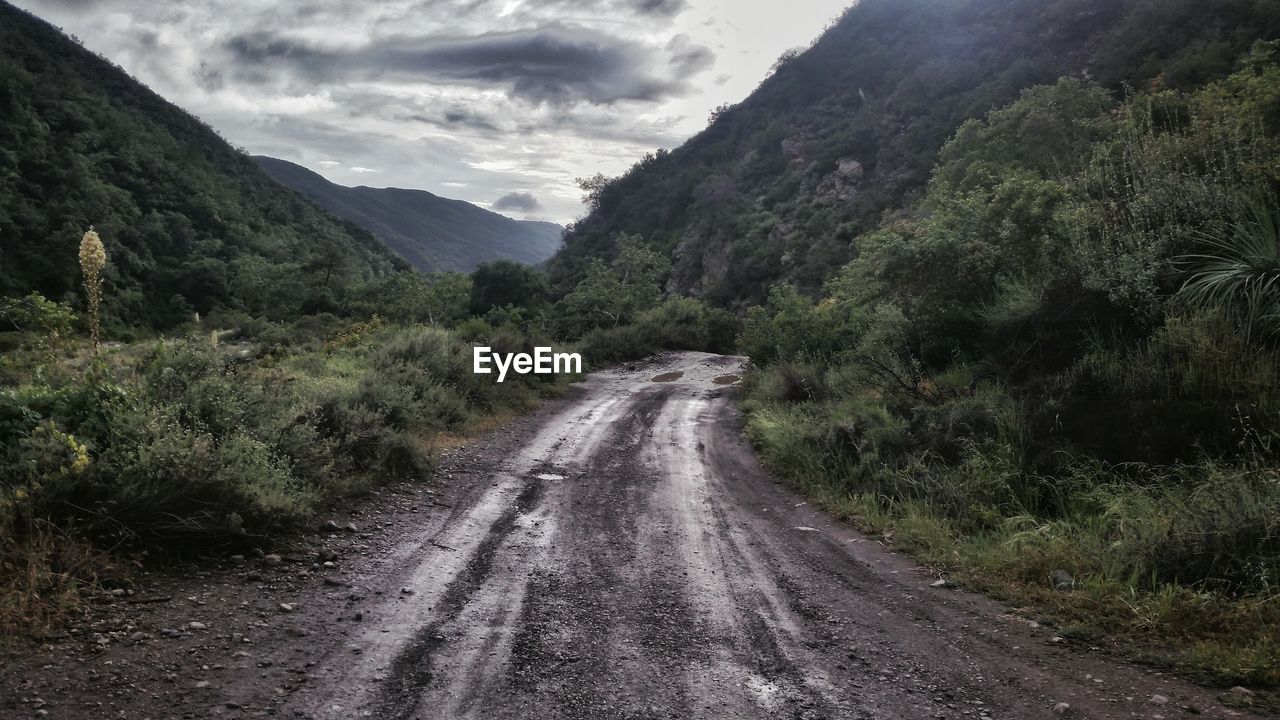 Empty dirt road leading towards mountains