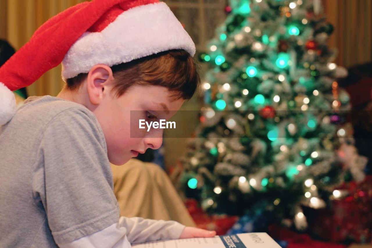 Close-up of boy reading book with illuminated christmas tree in background