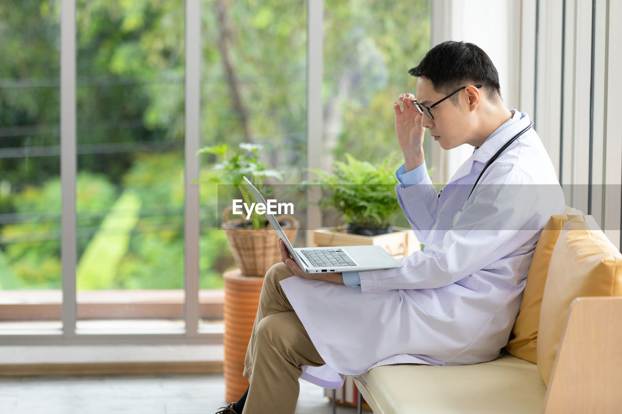 YOUNG MAN USING MOBILE PHONE WHILE SITTING ON LAPTOP AT HOME