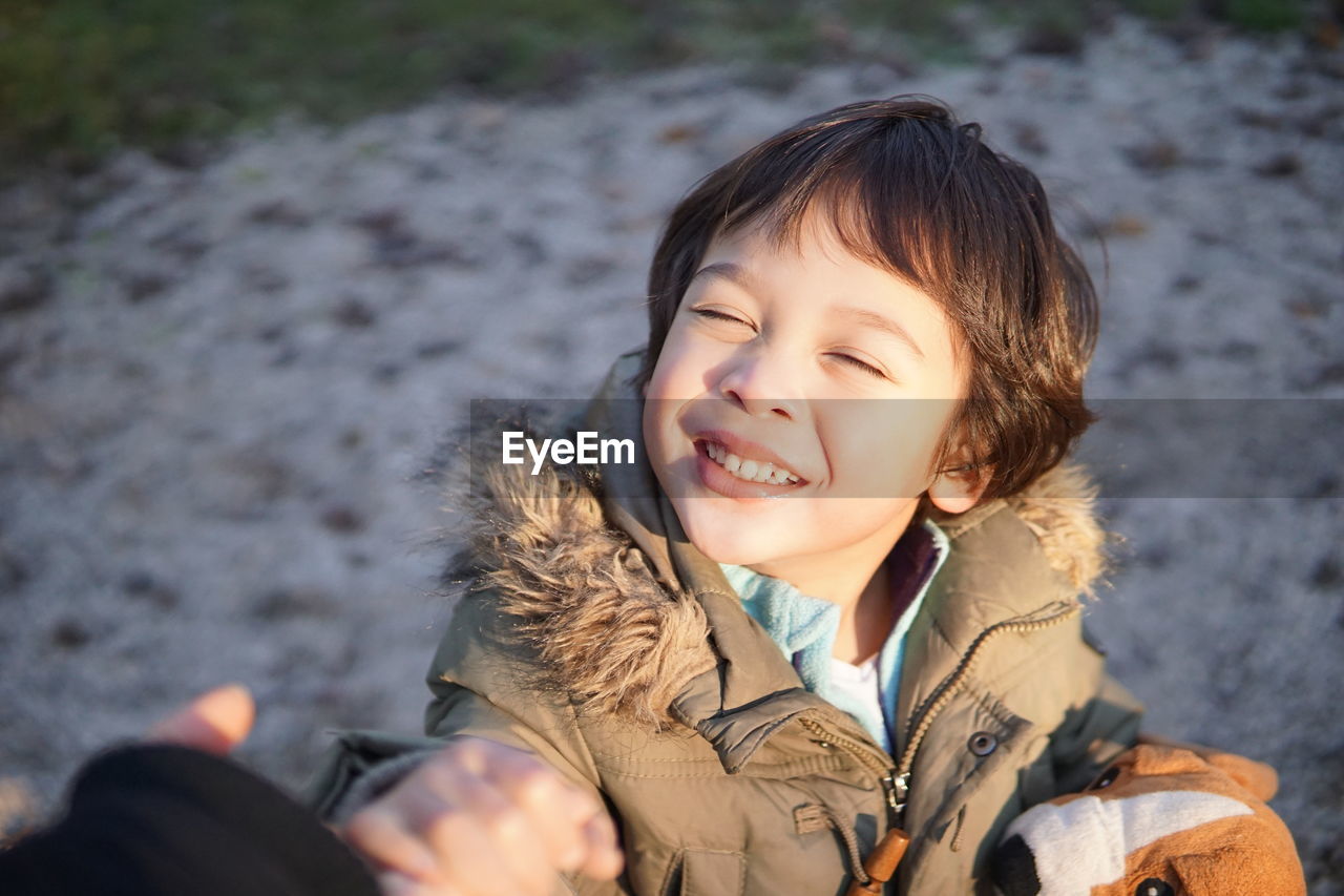 High angle view of cute smiling boy with eyes closed standing on snowy field