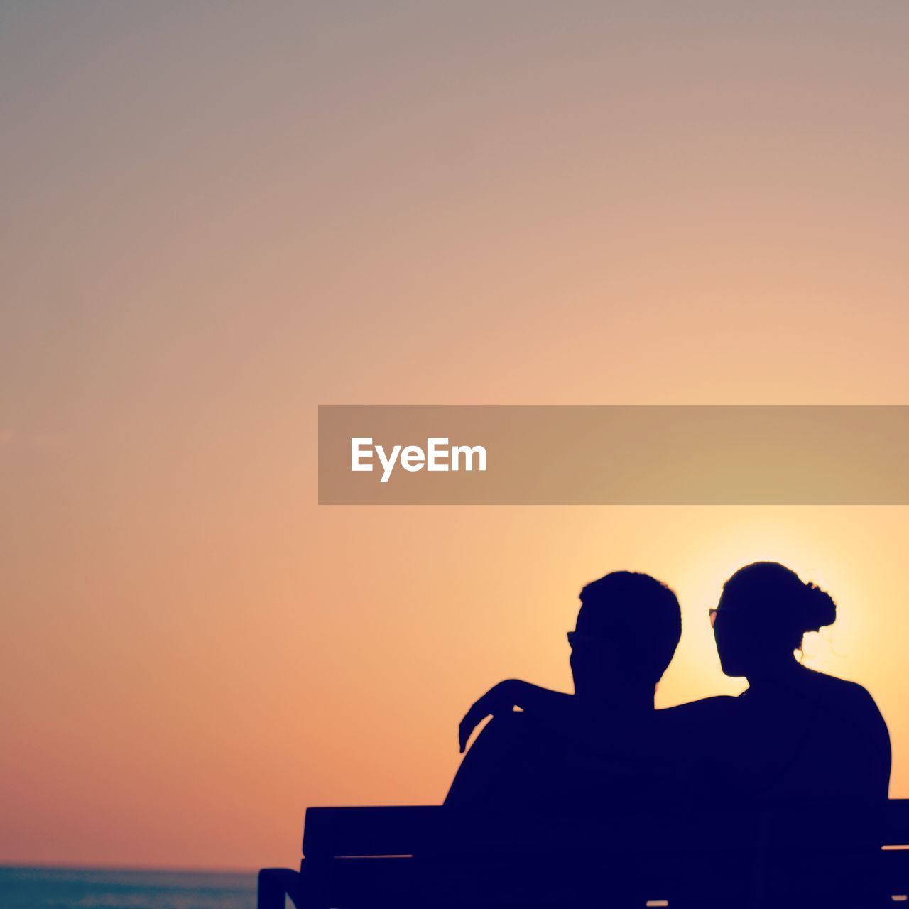 Rear view of silhouette couple sitting on bench against clear sky
