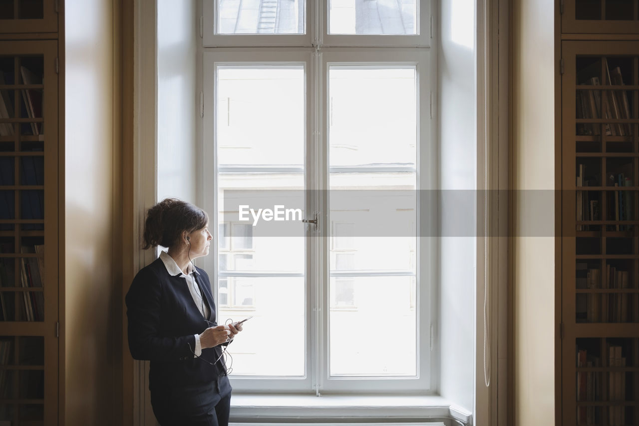 Female professional listening music while looking through window at library