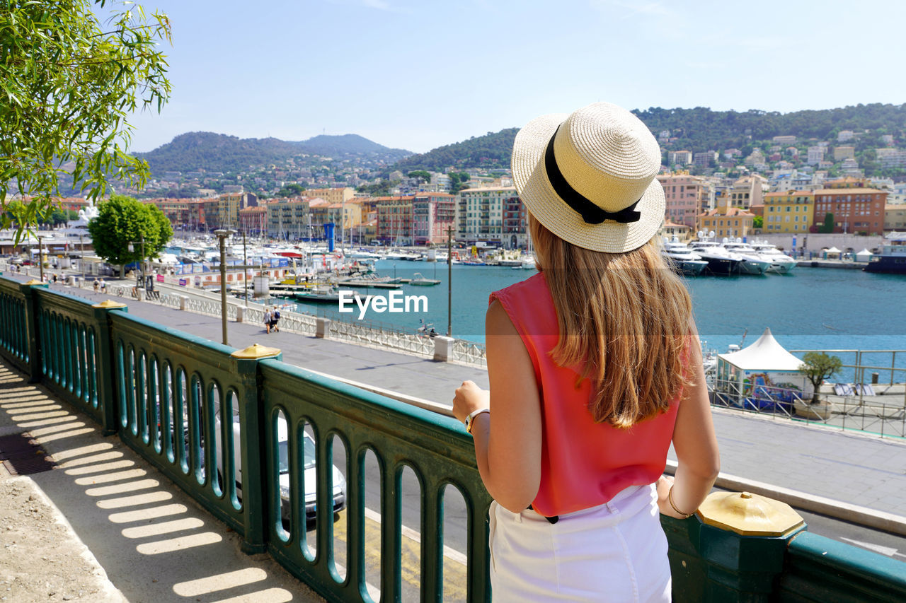 Beautiful young woman walks along nice seafront with lympia port, french riviera