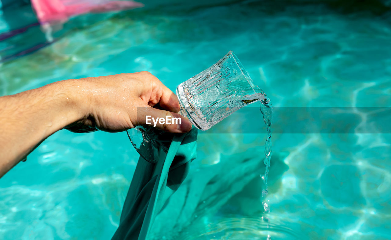 Cropped hand of men pouring drinking water in swimming pool
