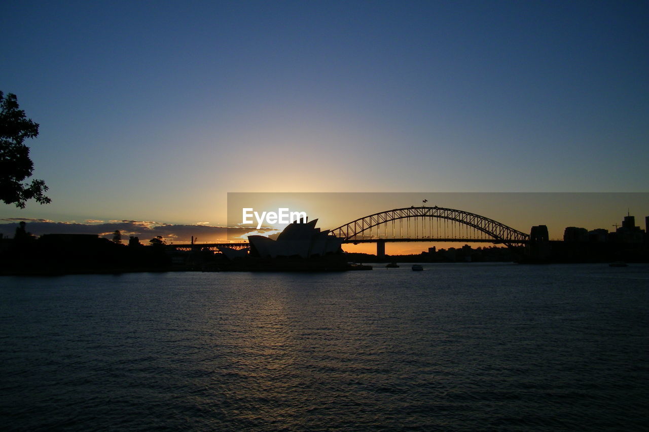 Silhouette bridge over harbor during sunset