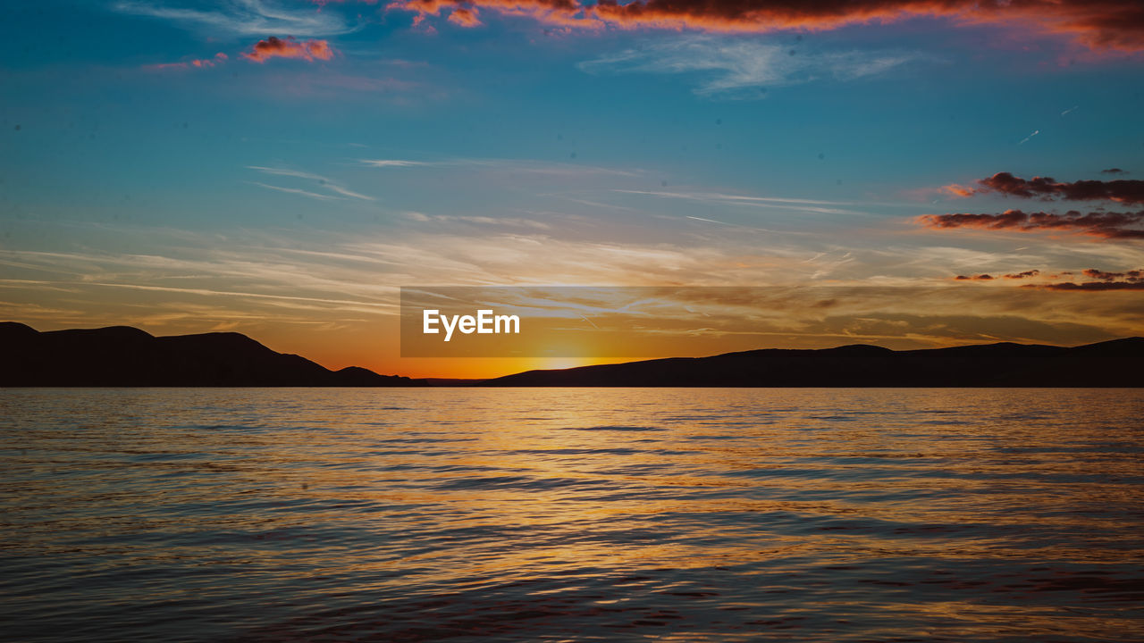 sky, water, sunset, beauty in nature, scenics - nature, sea, horizon, mountain, cloud, nature, afterglow, tranquility, ocean, evening, dawn, tranquil scene, environment, reflection, dramatic sky, landscape, land, coast, sunlight, seascape, no people, travel destinations, mountain range, idyllic, sun, shore, outdoors, travel, orange color, red sky at morning, beach, vacation, silhouette, trip, holiday, multi colored