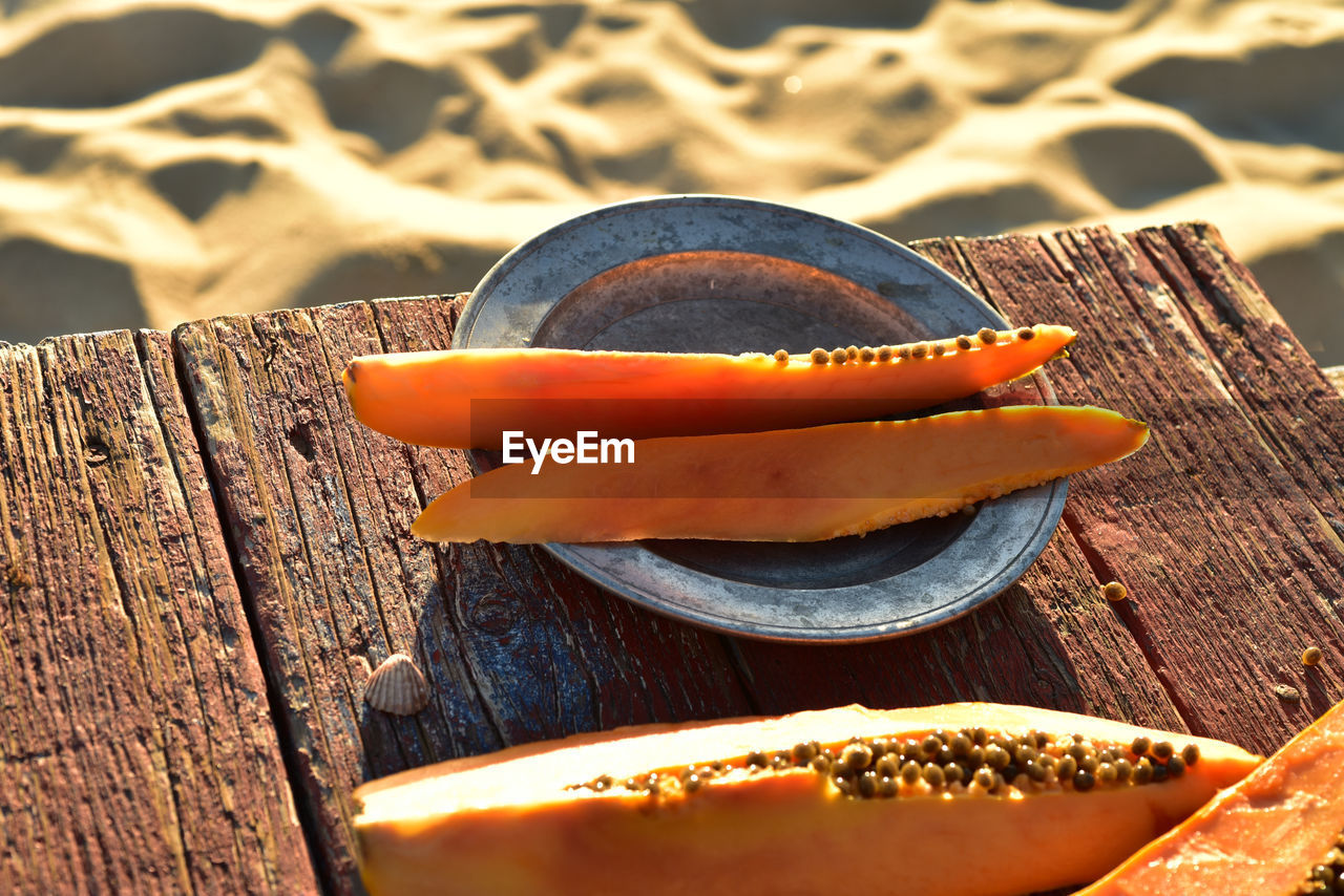 Fresh papaya slices on pewter plate on rustic wood table on sand beach  sea of cortez baja, mexico