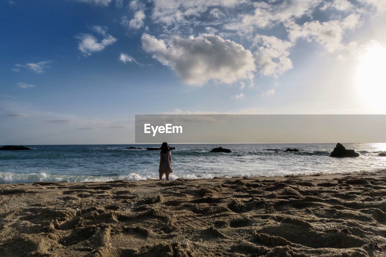 Girl standing at beach against sky during sunset