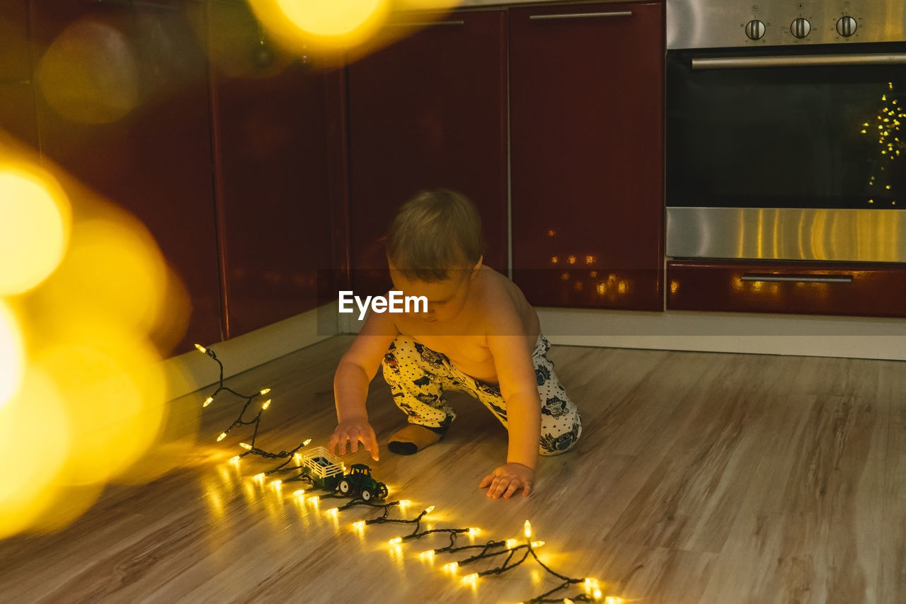 Full length of cute boy sitting by illuminated lights on floor