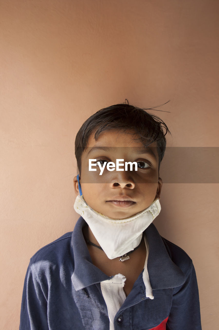 Portrait of boy wearing flu mask standing against wall