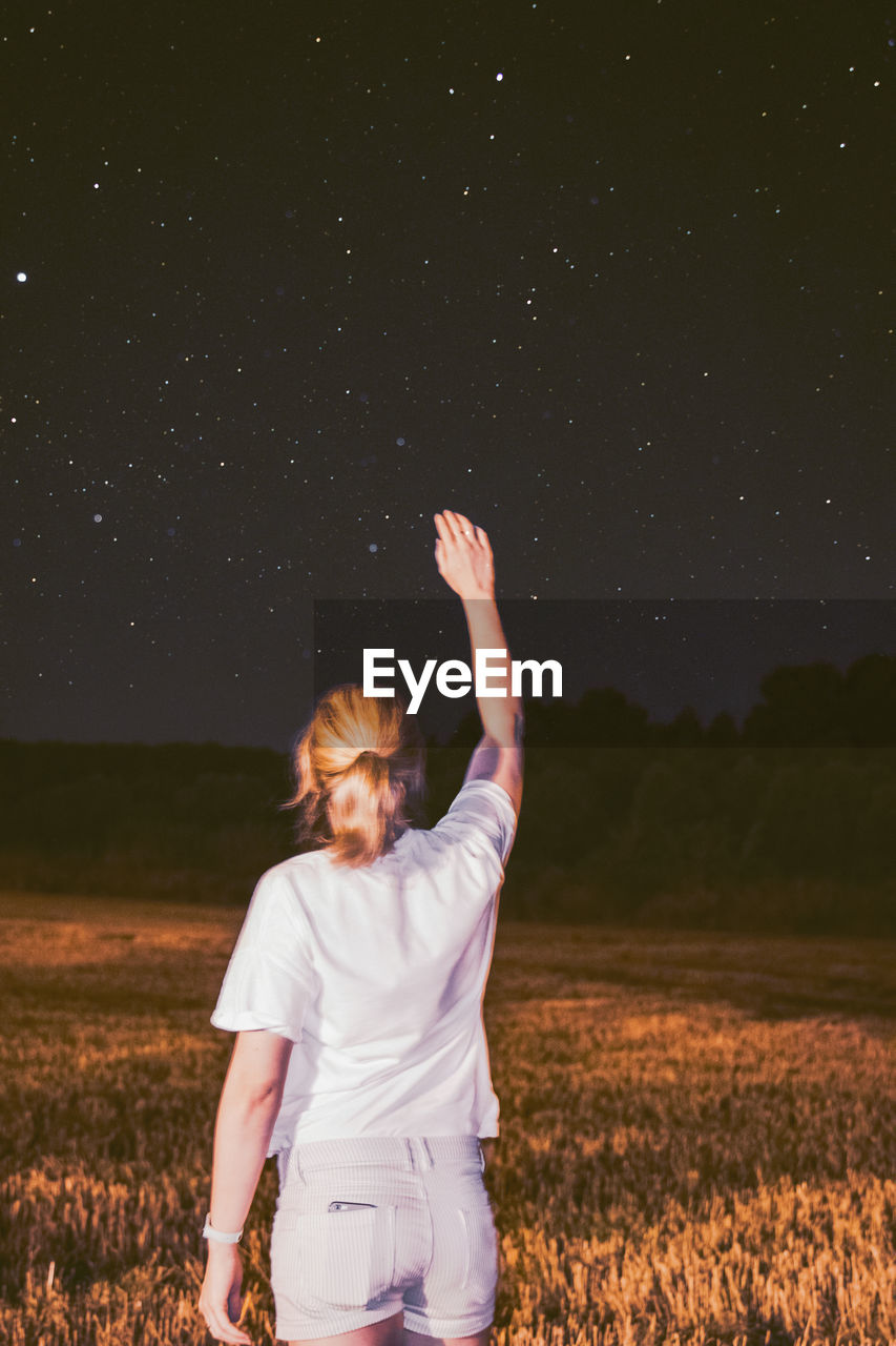 Rear view of woman standing on land against sky at night