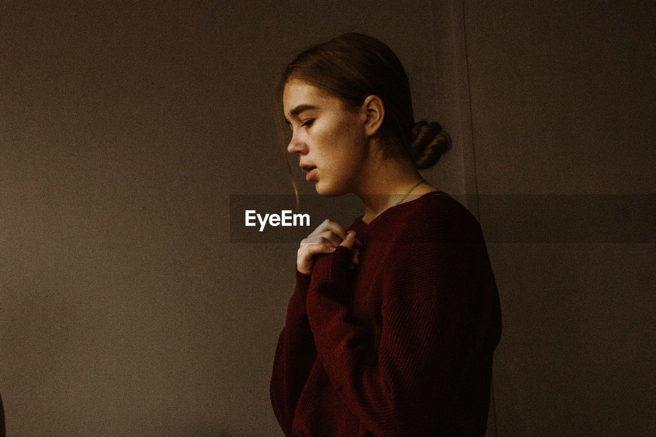 Side view of young woman looking away against wall