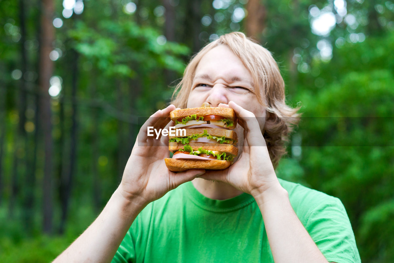 Young man holding piece big sausage sandwich on plate. student eats fast food