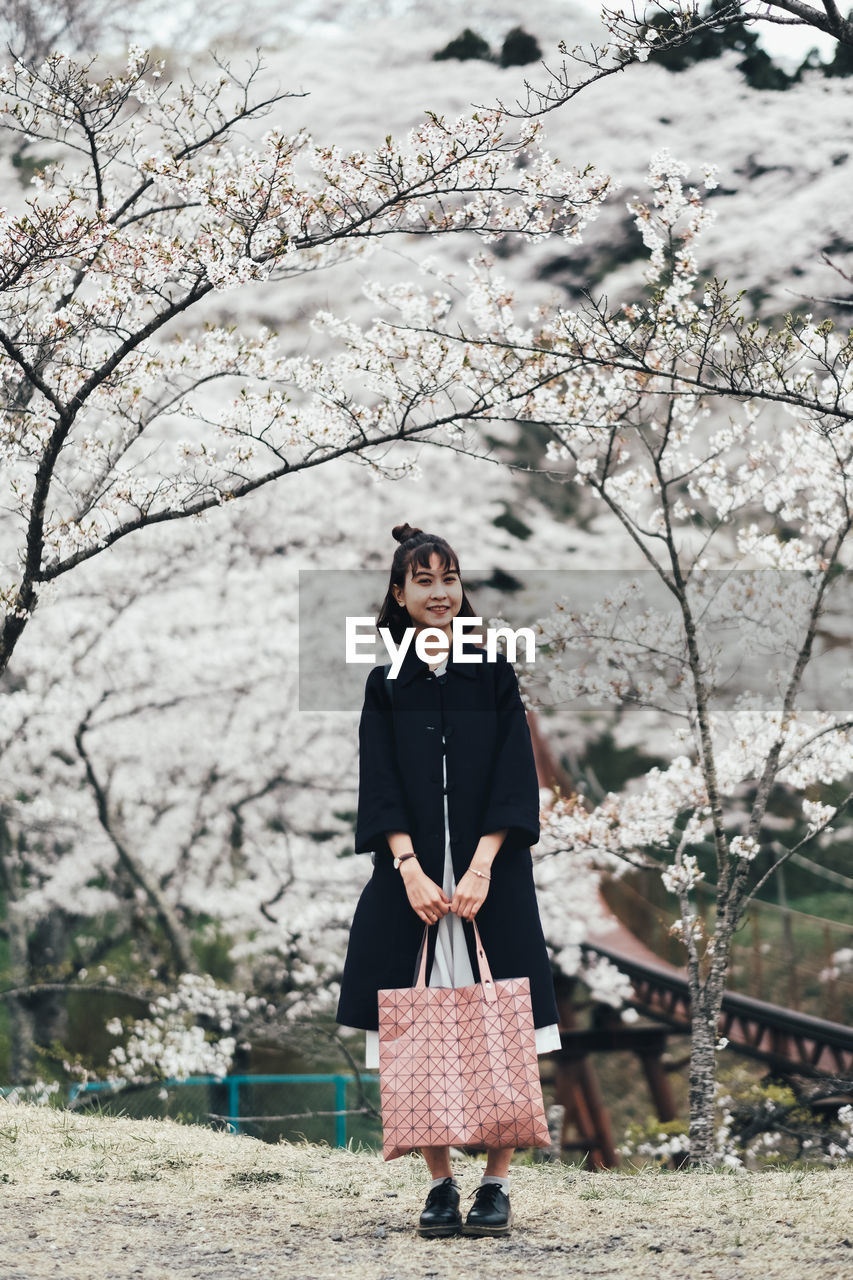 Full length of woman standing against cherry blossom trees