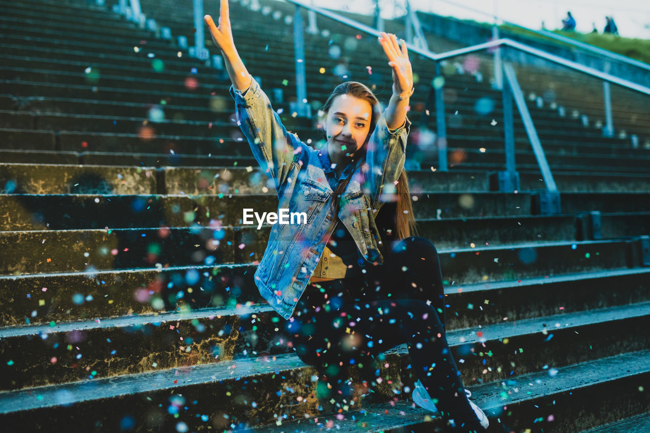 Portrait of woman throwing confetti while sitting on staircase