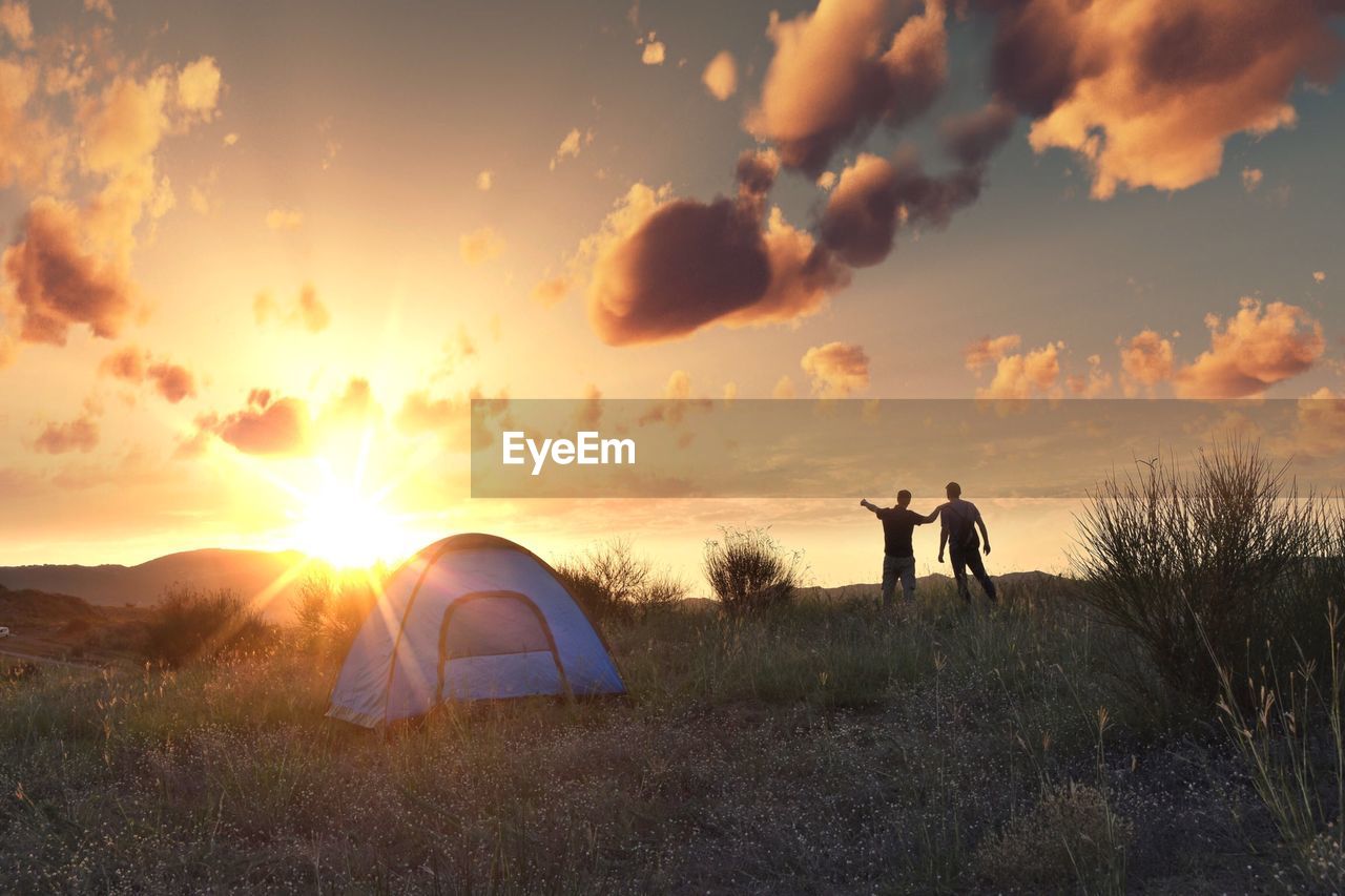 People standing on field by tent against sky during sunset