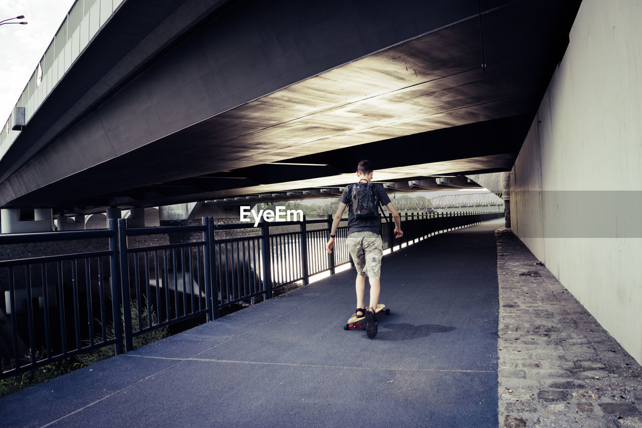 Rear view of man skateboarding on bridge