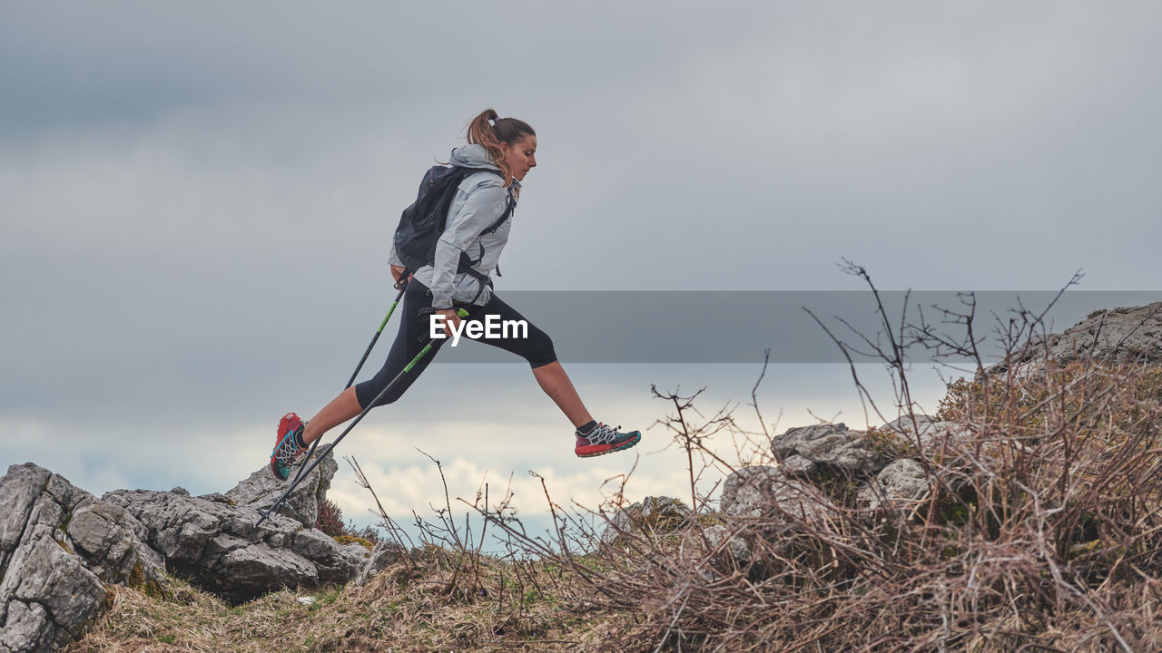 Sporty girl jumps between the stones during an alpine trekking