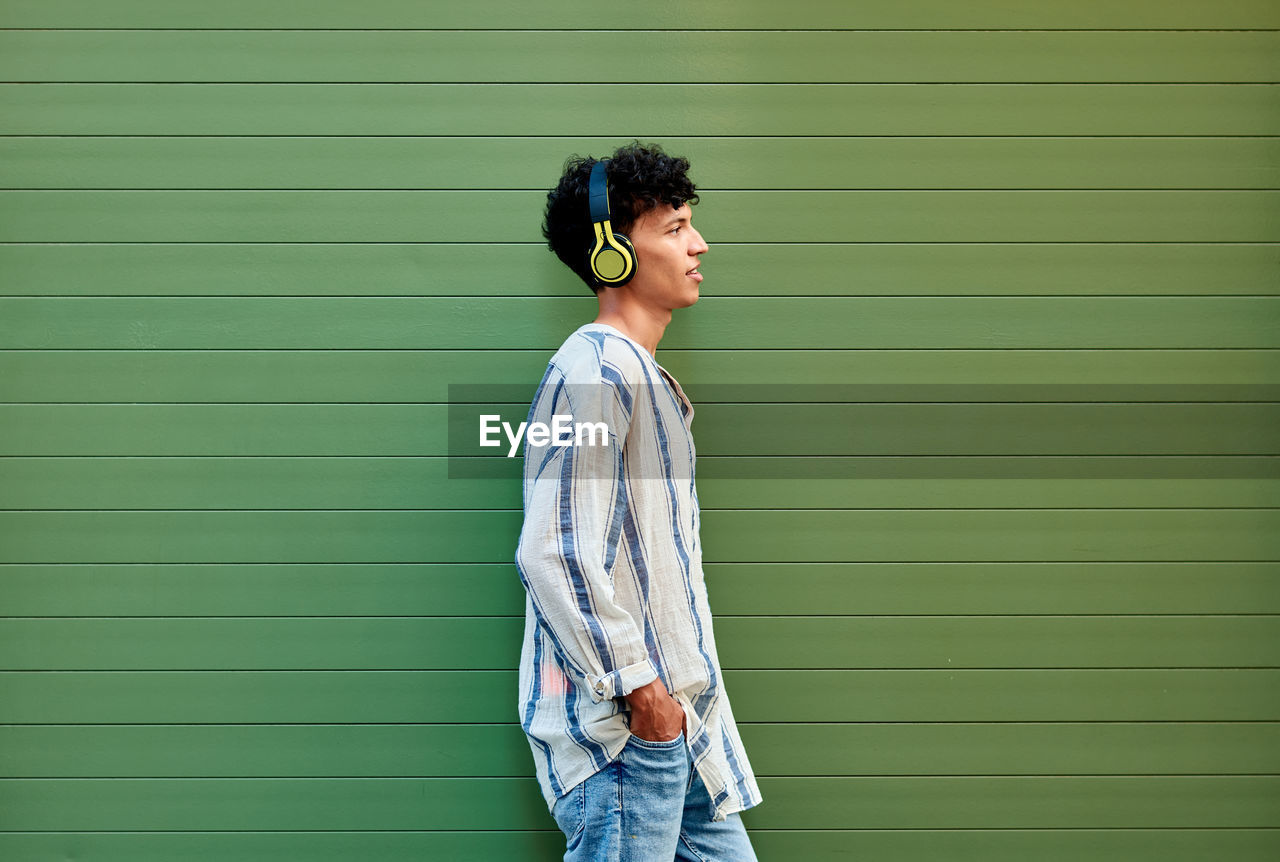 A young afro-haired man listens to music on a green background