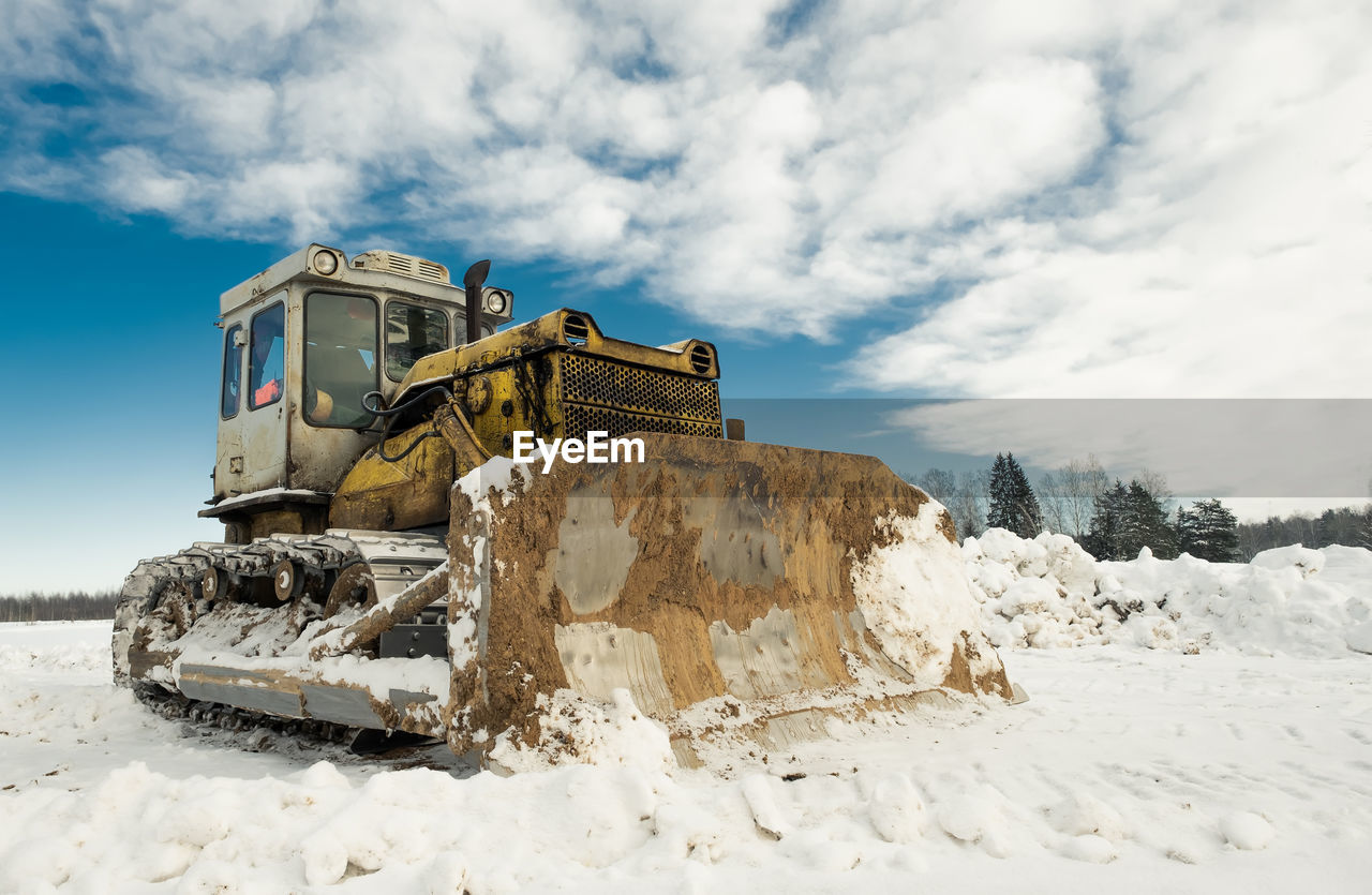 Yellow crawler tractor bulldozer with a bucket works in winter clearing the road from snow. 