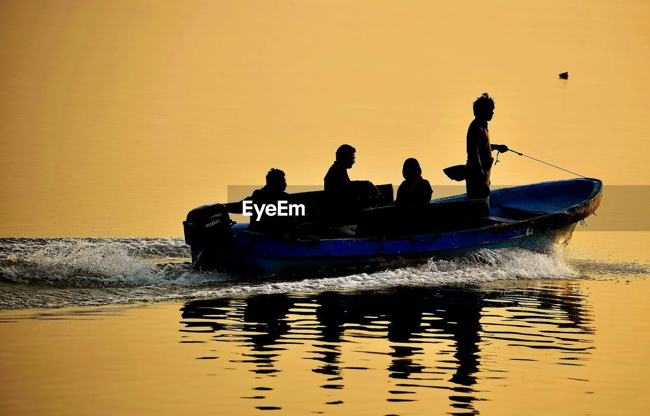 Silhouette people in little motor boat at sunset