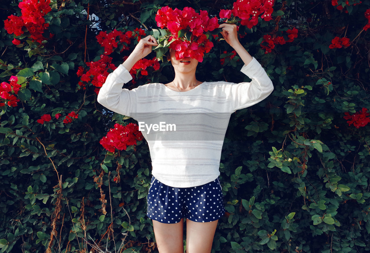 Young woman holding flowers while standing by plants in park