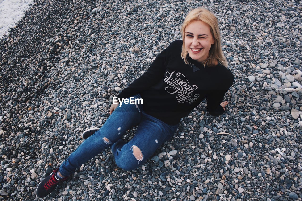 PORTRAIT OF YOUNG WOMAN SITTING ON COBBLESTONE