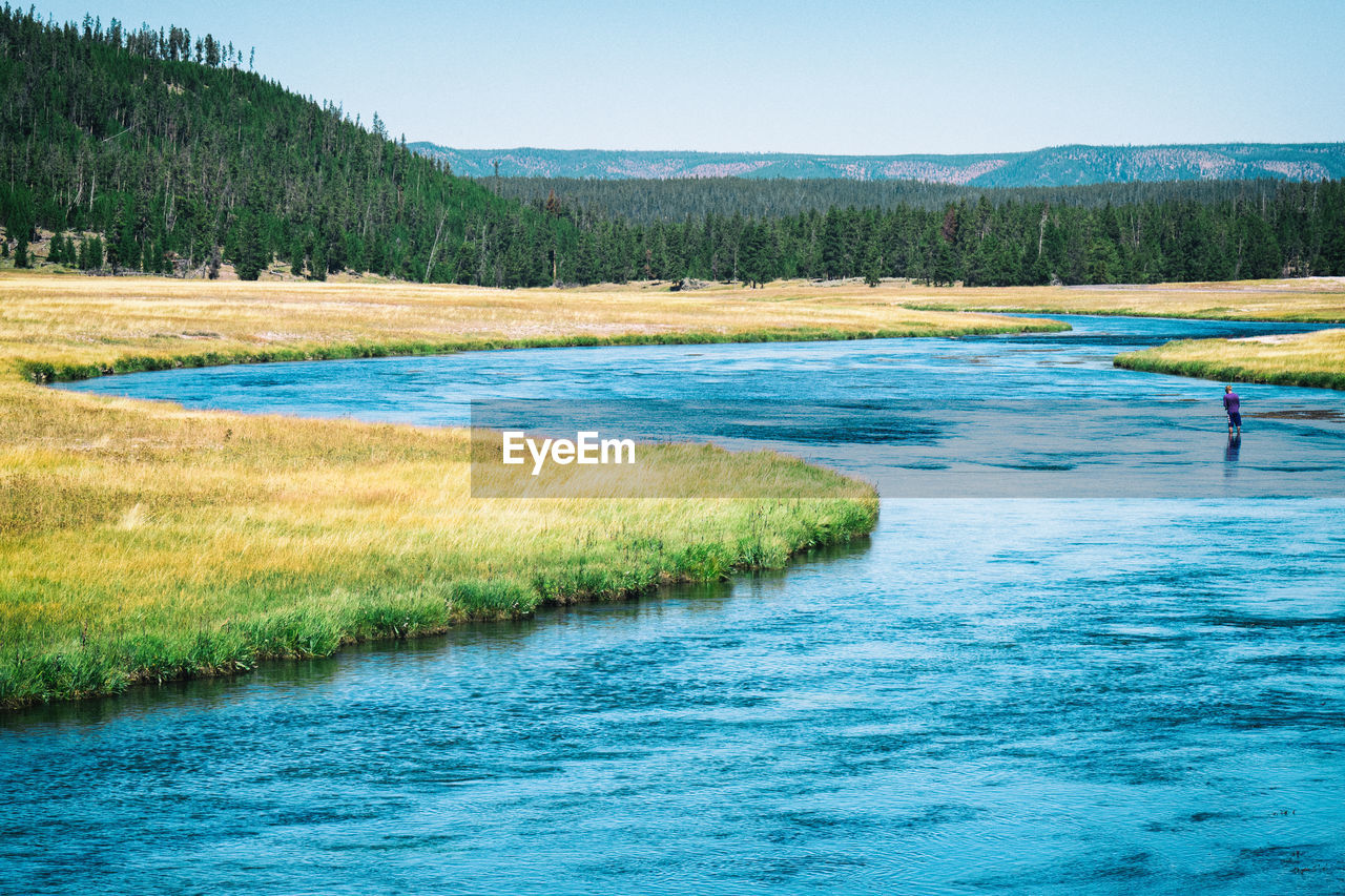 Man standing in a bending blue river fishing in yellowstone national park