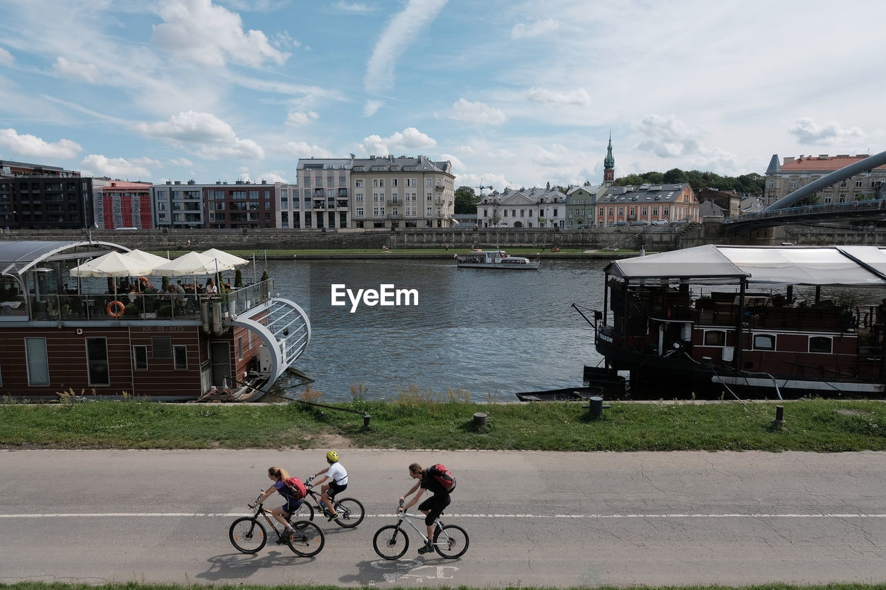 PEOPLE RIDING BICYCLE ON RIVER BY BUILDINGS IN CITY