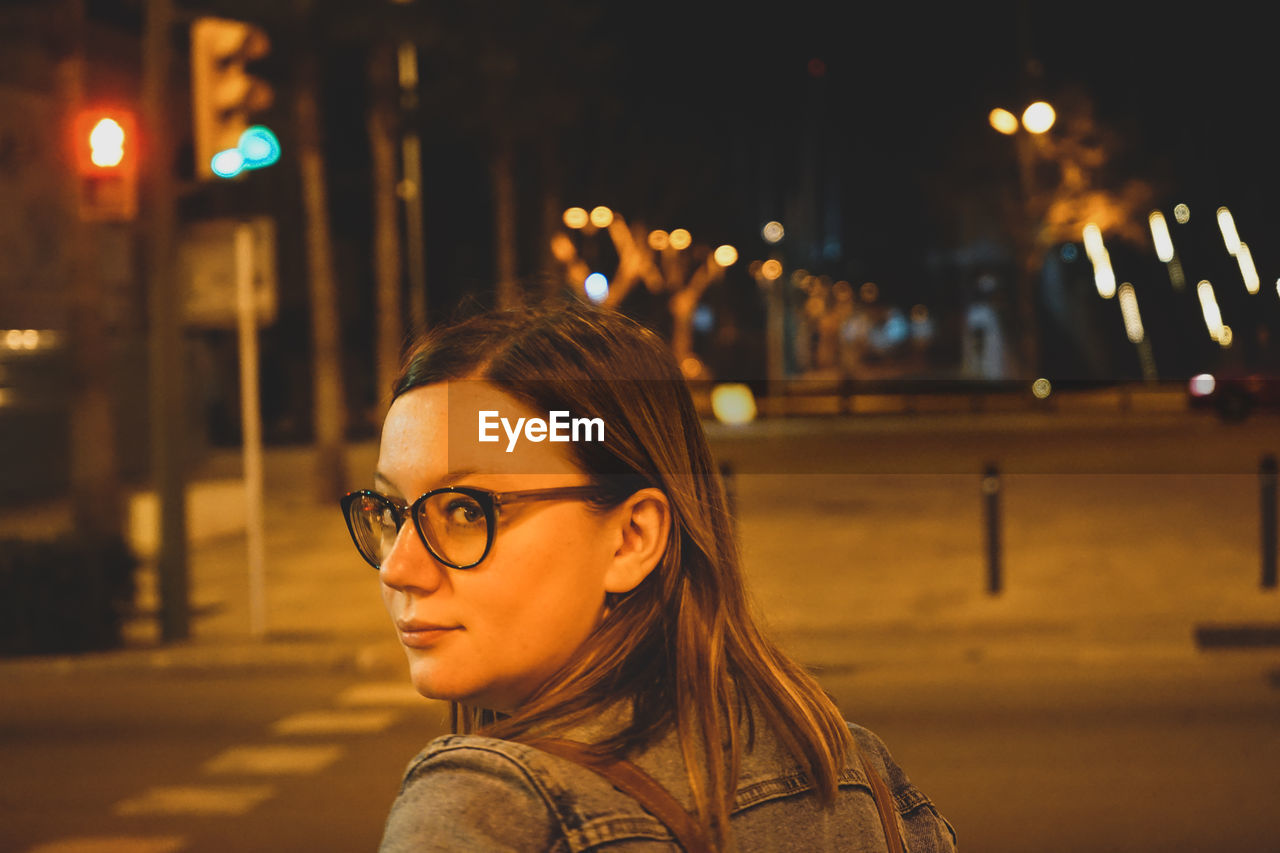 Portrait of woman on illuminated street in city at night