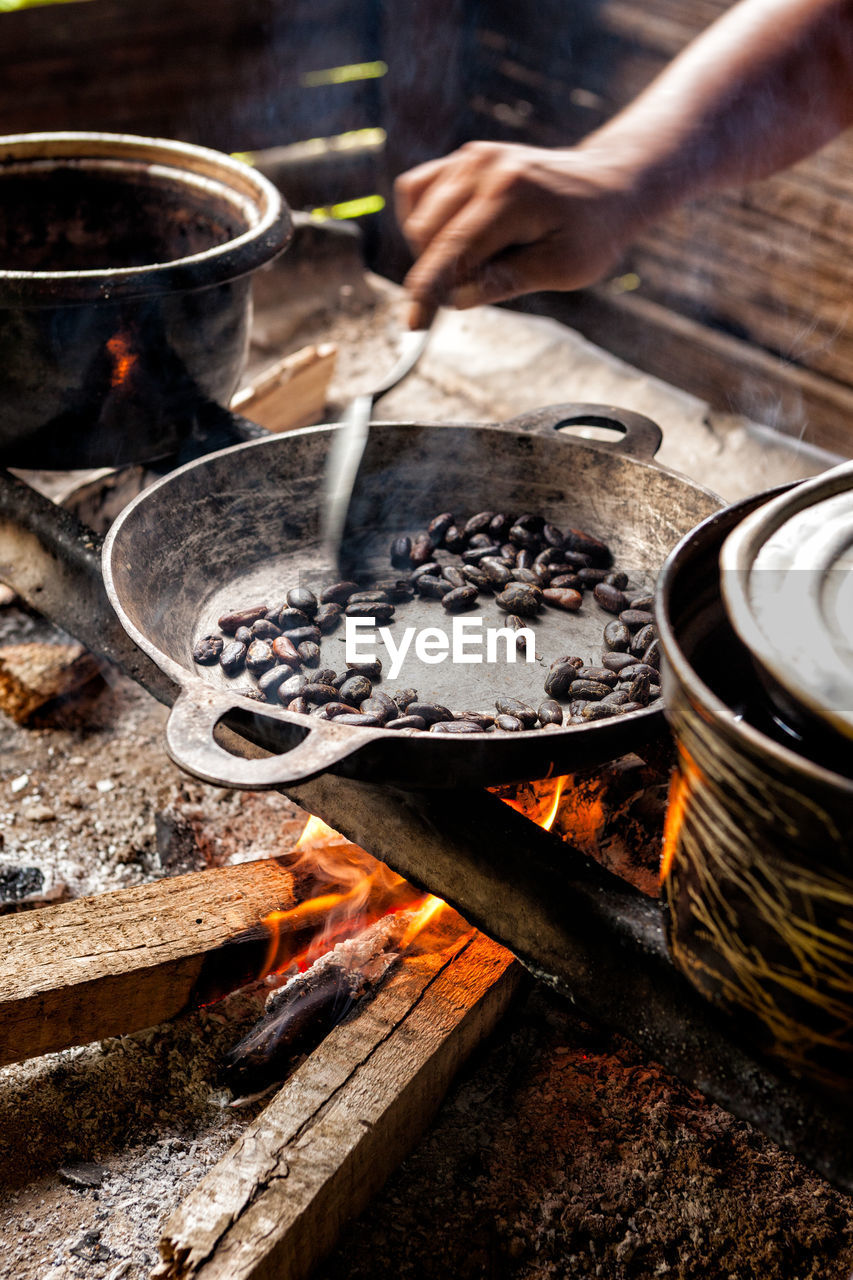 Close up of hand roasting cocoa bean on frying pan