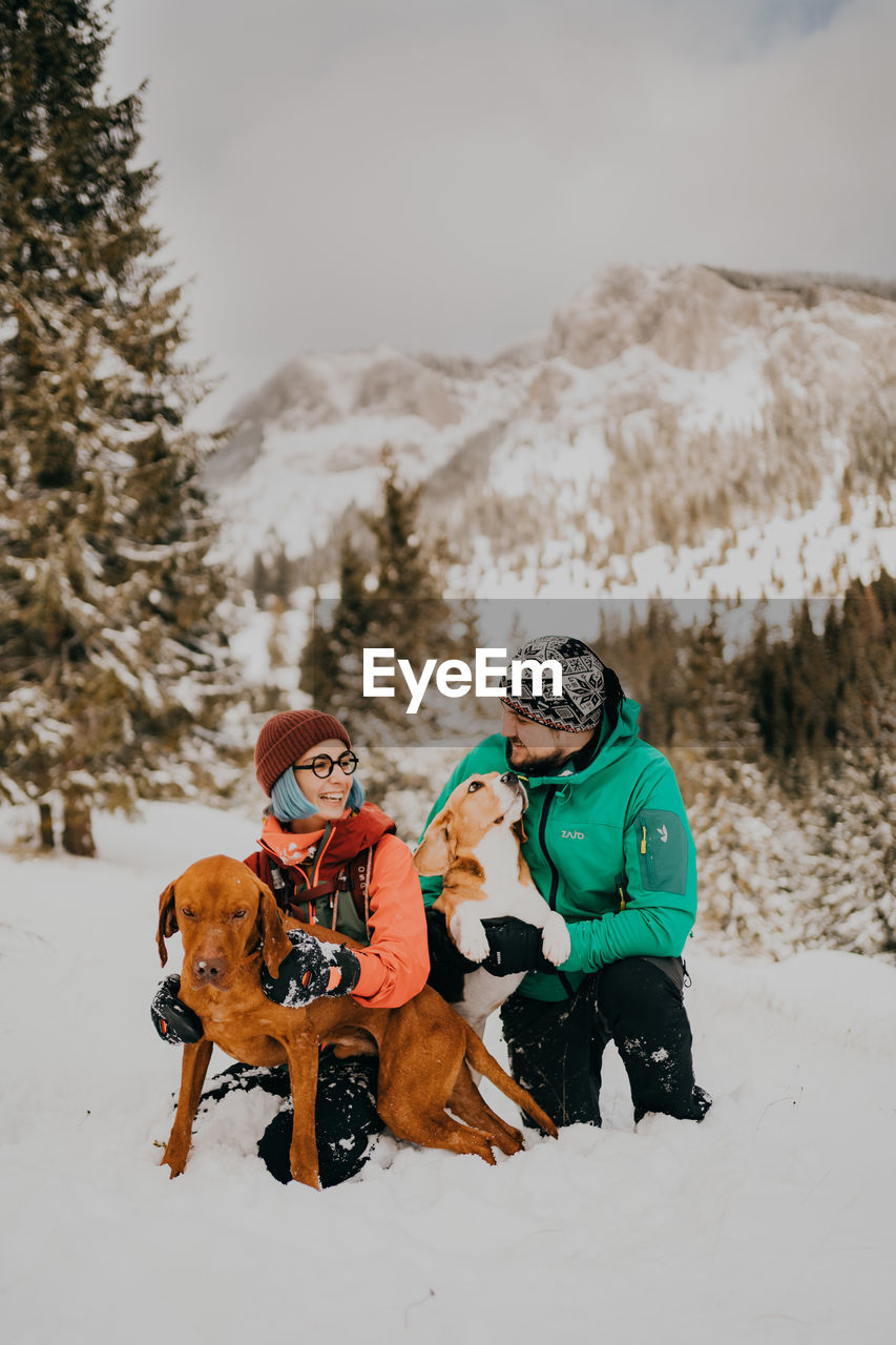 Portrait of couple with dogs on snow covered field