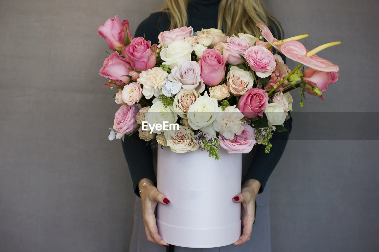 The beautiful bouquet of different roses in white box in female hands on gray background