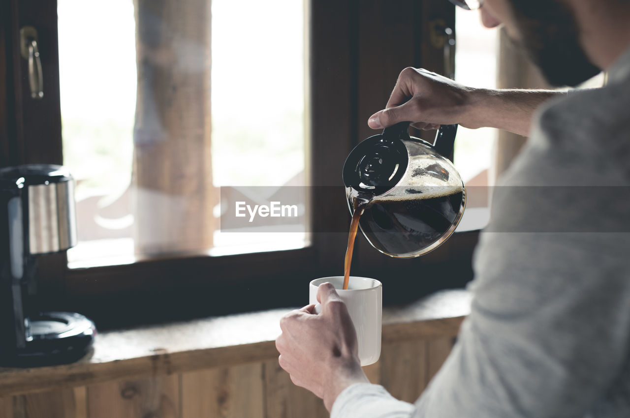 Young man pouring coffee into cup at home