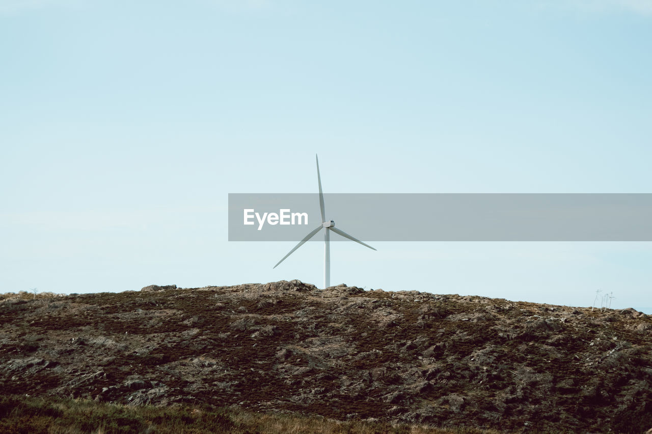 Low angle view of wind turbines on hill against sky