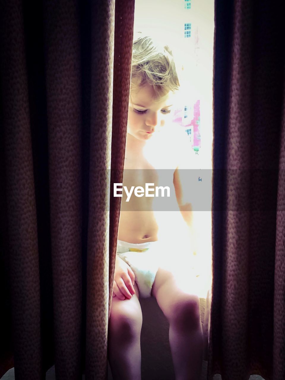 Little boy sitting in a window sill sunbathing 