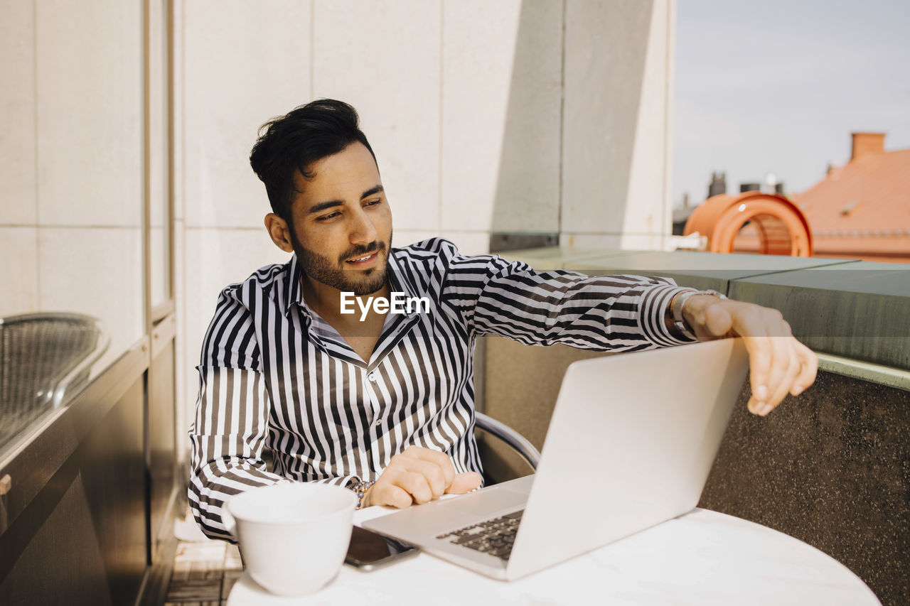 Young man using laptop while sitting in balcony at hotel