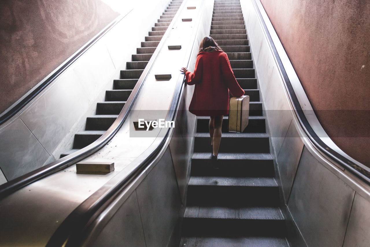 Rear view of woman with luggage on escalator in subway