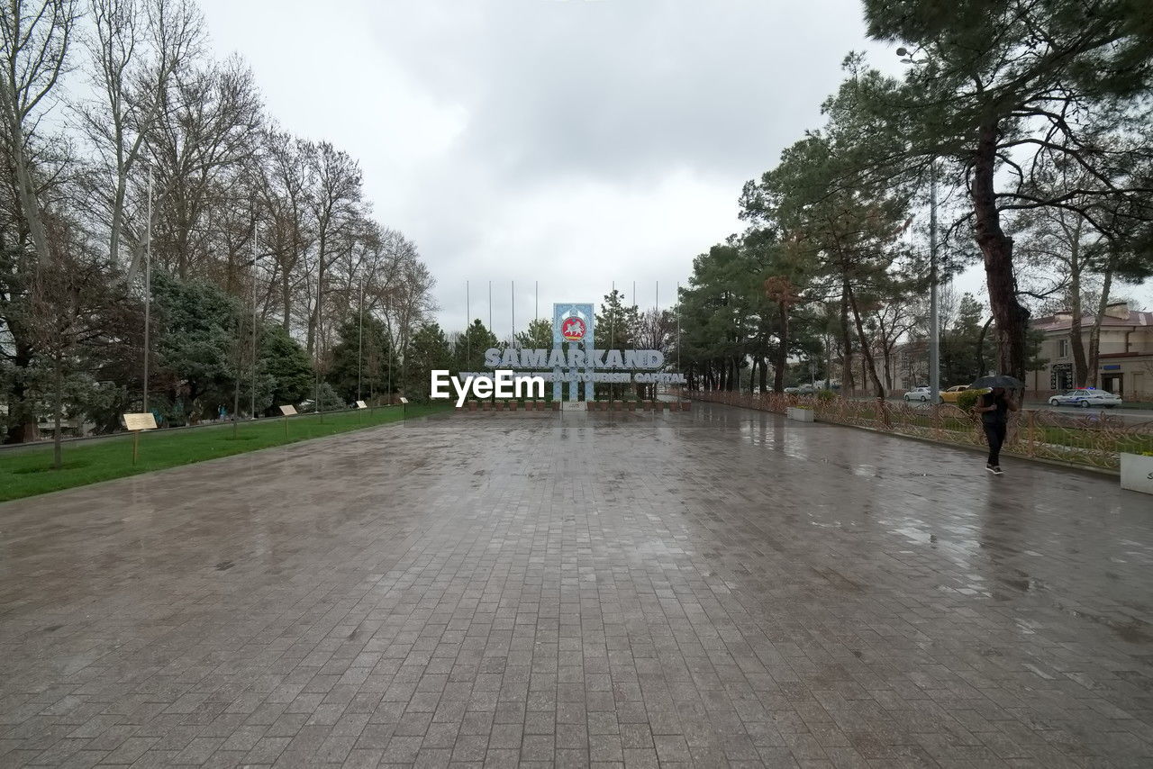 tree, plant, sky, cloud, architecture, nature, walkway, built structure, city, day, building exterior, outdoors, park, travel destinations, overcast, rain, town square, park - man made space, travel, wet, tourism, no people, road surface, building, street, water, public space