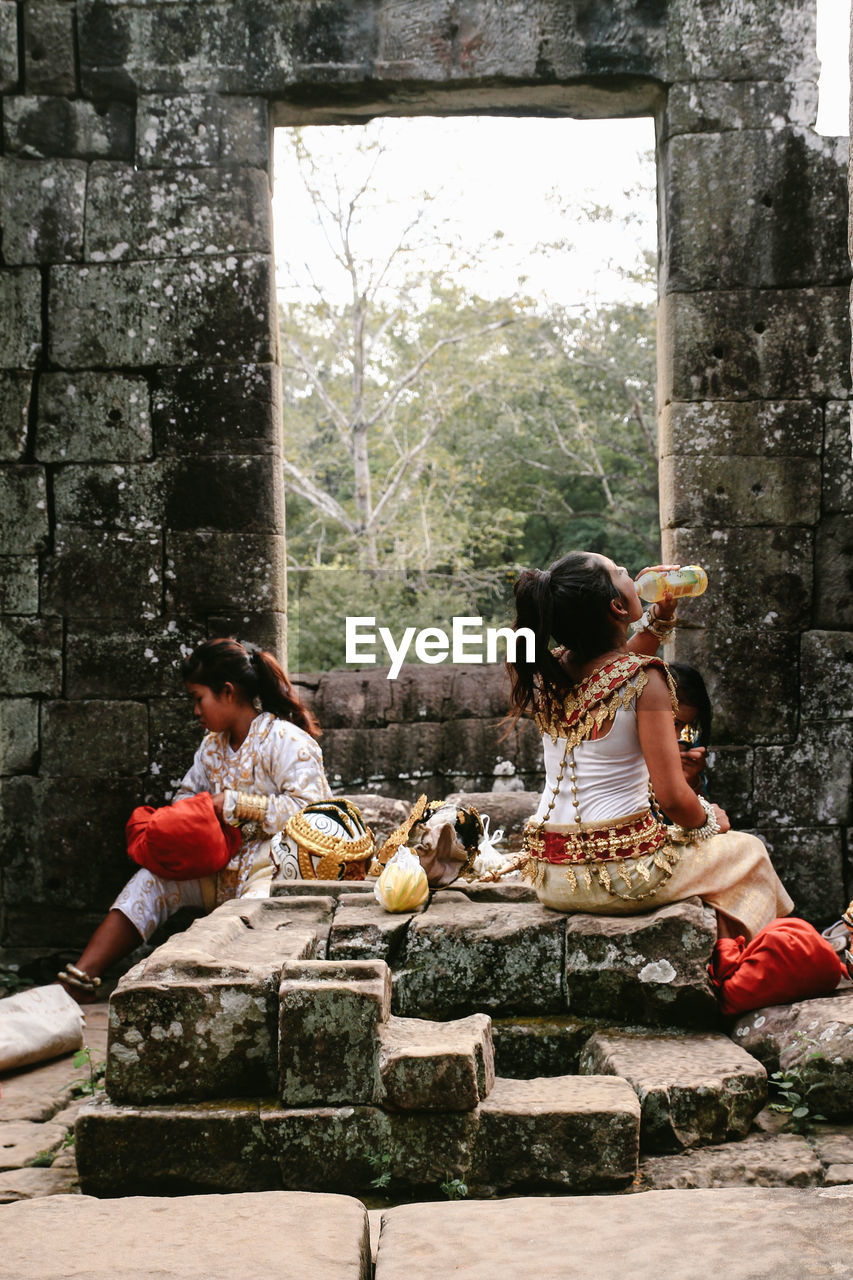 WOMEN SITTING ON STONE WALL WITH ARMS OUTSTRETCHED