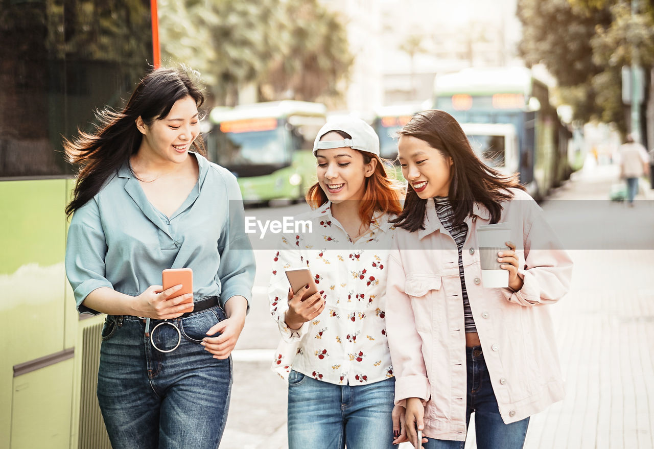 Cheerful young friends using phone in city 