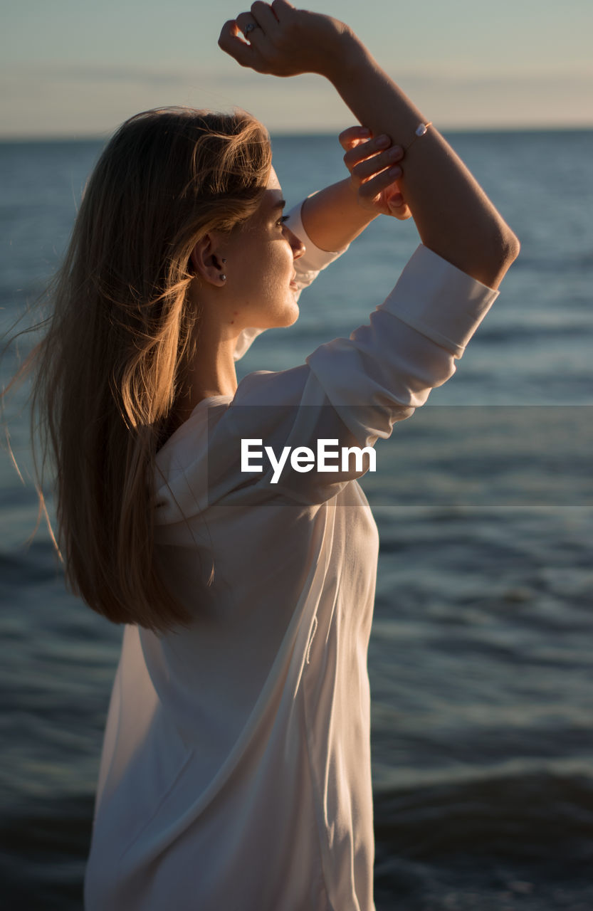 Young woman shielding eyes while standing by sea