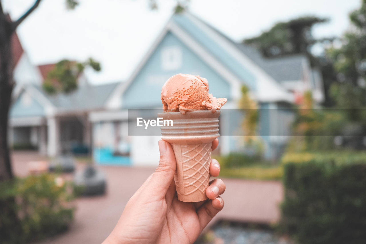 Cropped hand holding ice cream cone against house