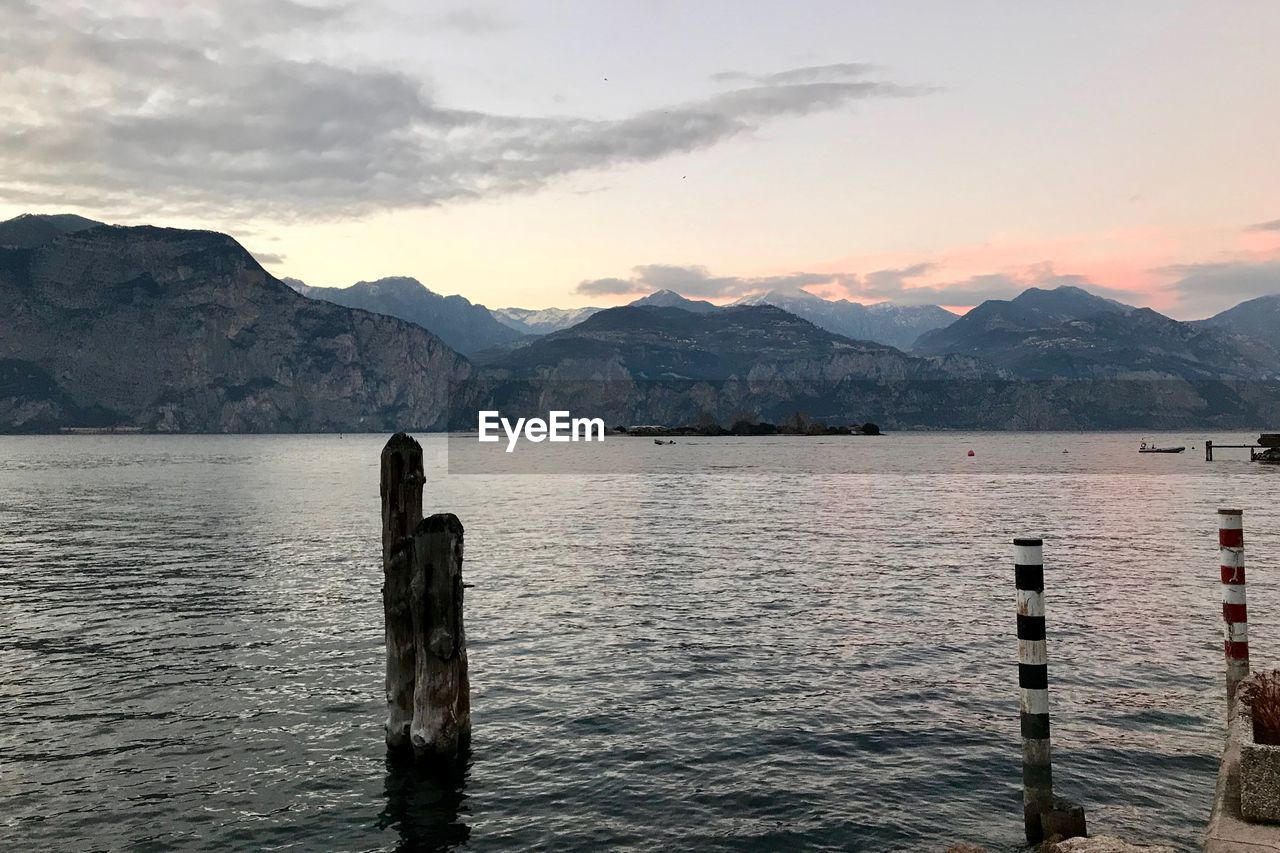 WOODEN POST IN LAKE AGAINST SKY DURING SUNSET