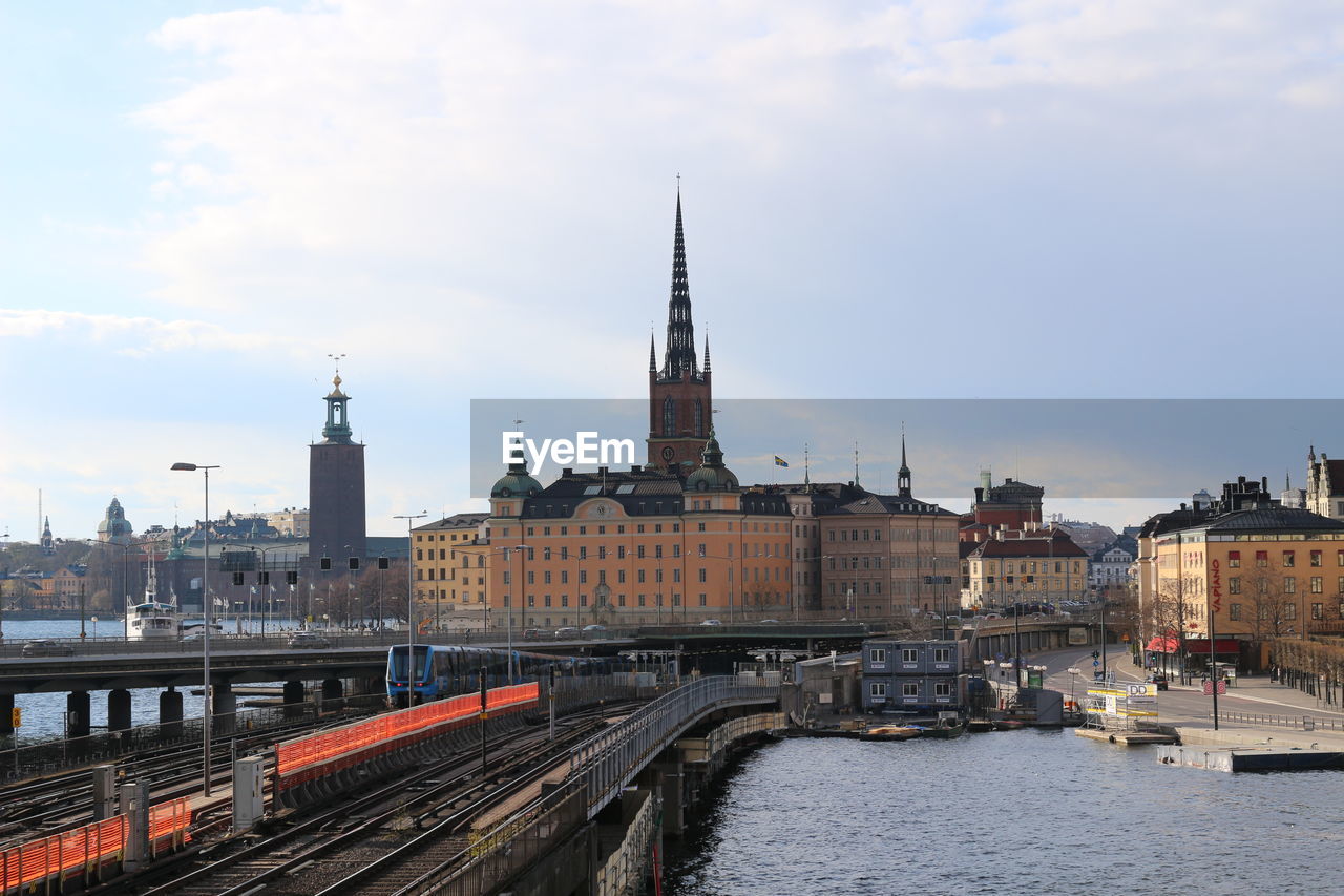 RIVER IN CITY AGAINST CLOUDY SKY