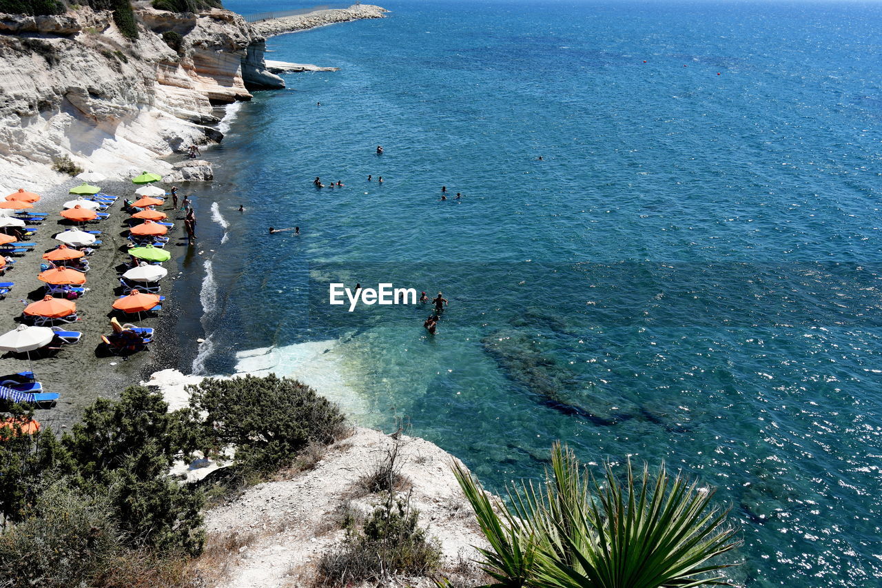 HIGH ANGLE VIEW OF GROUP OF PEOPLE ON ROCK BY SEA